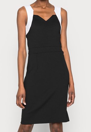 Robe noire ajustée avec des bandes blanches, présentant un décolleté en V et des coutures structurées. Le tissu a une texture lisse et une coupe mi-genoux.