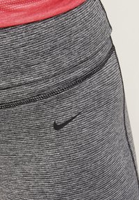 Czarne i szare legginsy sportowe o teksturowanym wykończeniu, z widocznym czarnym logo Nike i kontrastowymi detalami przeszyć.
