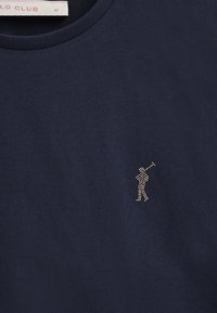 Granatowa bawełniana koszulka z okrągłym dekoltem; z metalowym, nabijanym logo golfisty na lewej piersi. Miękka struktura, dopasowany krój.