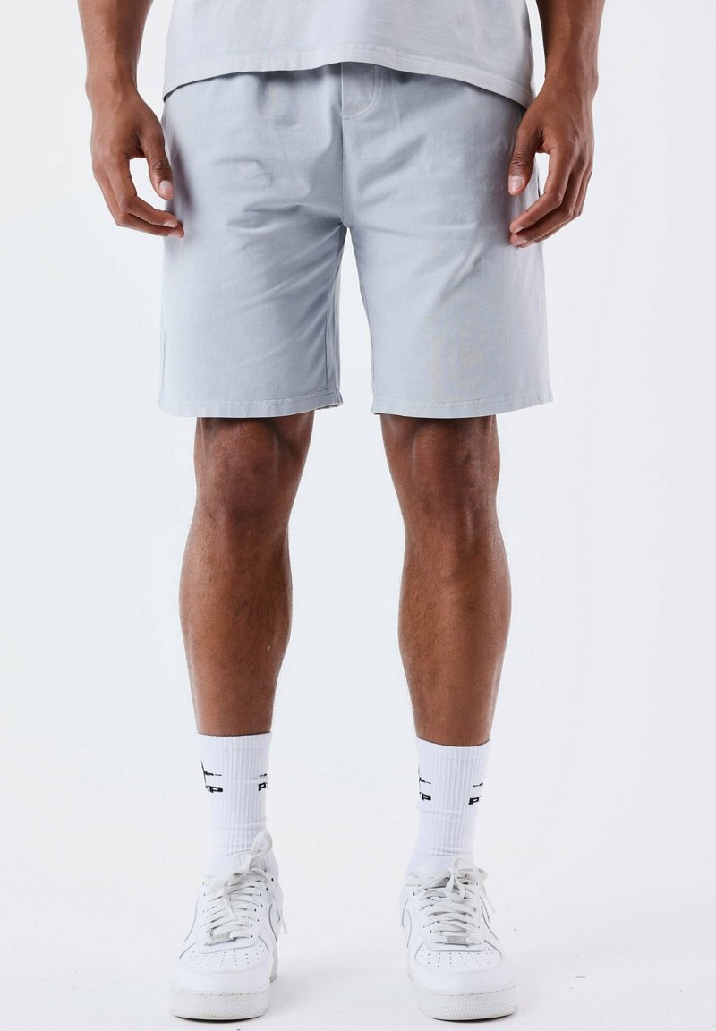 Pantalones cortos de algodón gris claro con corte recto, cinturilla elástica y bolsillos laterales, combinados con zapatillas deportivas blancas y calcetines.
