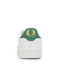 Witte sneaker met een glad leren bovenwerk, groene heelcounter en een gouden laurierembleem aan de achterkant. Rubberen zool, minimalistisch ontwerp.