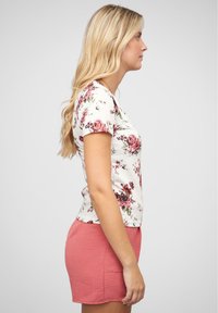 Haut à manches courtes à imprimé floral blanc avec des roses roses et bordeaux, associé à une jupe texturée rose clair. Vue de profil indépendante.