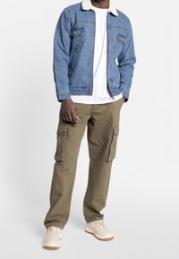 Jeansjack met sherpa-kraag, blauwe stof, ritssluiting aan de voorkant, gecombineerd met olijfgroene cargobroek met zijzakken en beige sneakers.