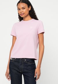 Tricou roz din bumbac, cu mâneci scurte, gât rotund și un mic logo pe piept. Asortat cu blugi de denim închisi la culoare.