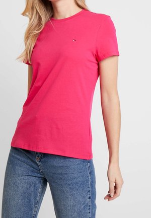 Vaaleanpunainen puuvillainen T-paita pyöreällä pääntiellä, lyhyillä hihoilla ja pienellä logolla rinnassa. Yhdistetty farkkuihin.