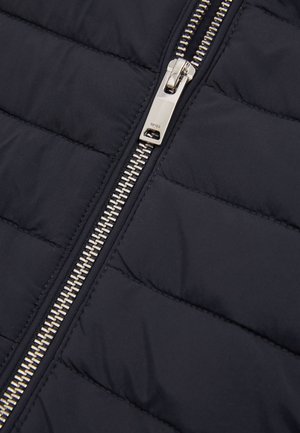 Hõbedane metallist luku tõmbaja mustal pitsatatud kangast jakil, millel on horisontaalsed õmblused, lähedalt.