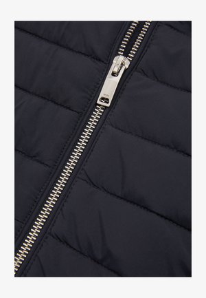 Hõbedane metallist luku tõmbaja mustal pitsatatud kangast jakil, millel on horisontaalsed õmblused, lähedalt.