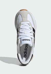 Biely športový topánok s čiernymi pruhmi a sivými semišovými akcentmi. Má viazací dizajn a textúrovanú podrážku. Logo Adidas na jazyku a vnútri topánky.