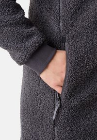 Grå fleecejacka med detaljer av texturerat tyg, sidoficka med dragkedja och elastiska muddar. Fokus på värme och komfort.