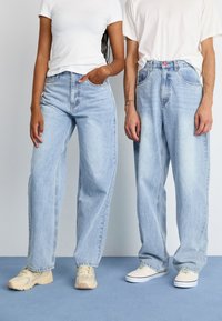 Lyseblå denimjeans med løs passform, frontlommer og falmet tekstur. Kombinert med hvite t-skjorter og beige sneakers.