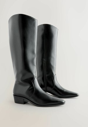 Sorte knæhøje støvler lavet af skinnende kunstlæder. Spidse tæer med en lav blokhæl og en sidelukning for nem påtagning. Glat tekstur.