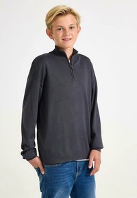 Dark gray pullover with a half-zip collar, relaxed fit, long sleeves, and ribbed cuffs, worn over blue jeans. Smooth texture.