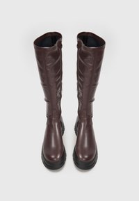 Bottes en cuir marron, montantes jusqu'au genou, avec une finition lisse, dotées d'une semelle en caoutchouc noire et de zips latéraux pour un enfilage facile.