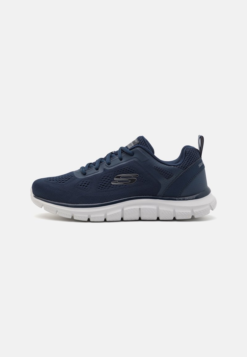 Baskets de sport bleu marine avec tige en mesh, fermeture lacée, semelle blanche segmentée et languette au talon, marquées du logo "S" sur le côté.