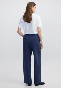 Navyblauwe wijde broek met een gladde textuur en een elastische tailleband, gecombineerd met een wit shirt met korte mouwen. Twee achterzakken zichtbaar.