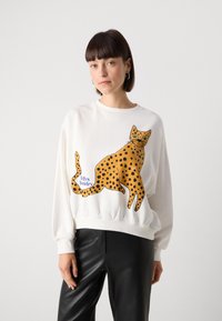 Felpa bianca con una grande illustrazione di un leopardo giallo maculato di nero. Polsini e fondo a coste, abbinata a pantaloni in pelle nera.