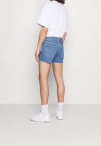 Jeansshorts, ljusblå, fransad fåll, femfickorsdesign, bärs med en vit t-shirt och vita sneakers med en subtil logotyp på ankelsockarna.