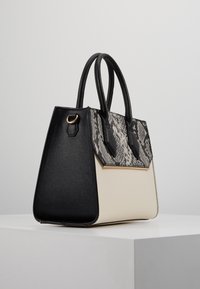Strukturert totebag i svart og krem, med en teksturert svart lærkropp og en mønstret slangeskinnslapp, samt to håndtak.