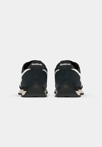 Sneaker in suede nero con dettagli bianchi, collarino imbottito e suola in gomma. Presentano un tallone testurizzato per una migliore aderenza e il marchio Reebok sul retro.