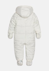 Bílý zateplený snowsuit s kapucí, vybavený ribkovanými manžetami, integrovanými palčáky a elastickými otvory na nohy. Hladká, lesklá textura.