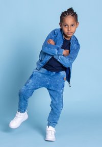 Niebieska kurtka dżinsowa i pasujące dresy z przetartym wzorem. Zestawione z białymi sneakersami za kostkę. Prosty, sportowy design.