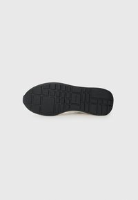 Zool van een sneaker met een zwart rubbermateriaal en een loopprofiel, met rechthoekige en vierkante indents voor grip.