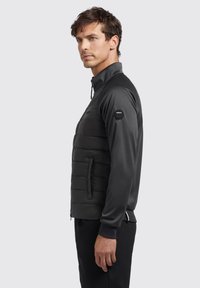 Black puffer jacket with a smooth finish, featuring a padded front, zippered pockets, and a high collar. Includes a logo on the sleeve.