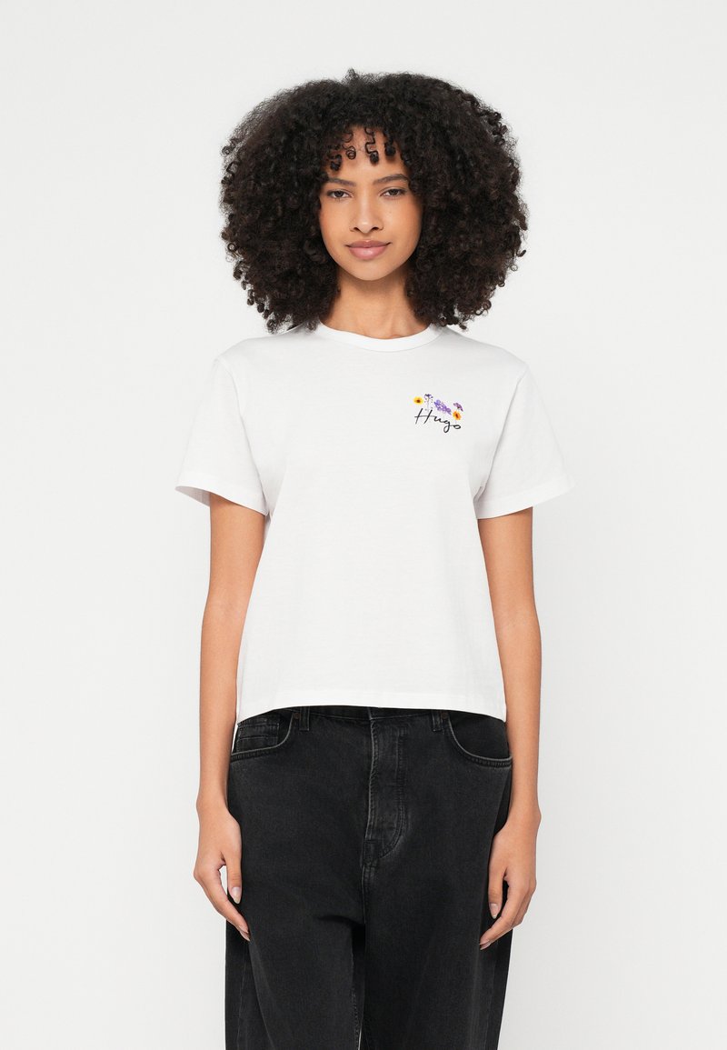 Λευκό βαμβακερό t-shirt με στρογγυλή λαιμόκοψη, κοντά μανίκια, με πολύχρωμη κεντητή λουλουδένια διακόσμηση και τη λέξη "Hug" σε μαύρη γραφή στο στήθος.