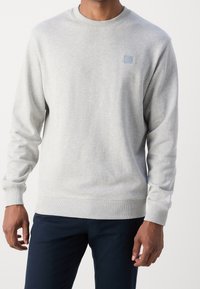 Szara bluza z ribbowanymi mankietami i dolnym brzegiem, z małym niebieskim kwadratowym logo na piersi. Gładka tekstura, klasyczny fason z okrągłym dekoltem.