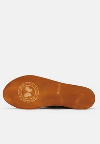 Plantilla de zapato de madera marrón con forma redondeada. Logo grabado y texto que dice "Hecho a mano con amor desde 1993". Textura suave, sin patrones.