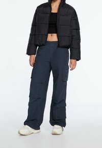 Zwarte pufferjas met horizontale stiksels, cropped ontwerp; gecombineerd met donkere cargobroek met meerdere zakken en een relaxte pasvorm.