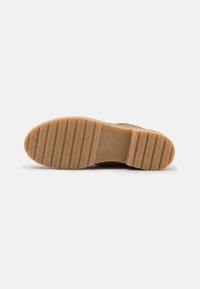 Suola di una scarpa marrone con battistrada in gomma texturizzata, caratterizzata da scanalature diagonali e orizzontali, posizionata su uno sfondo bianco semplice.