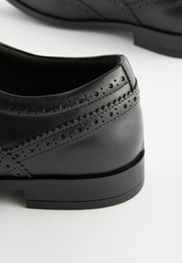 Zapatos de cuero negro con un acabado suave, que cuentan con perforaciones decorativas y un tacón bajo y apilado para mayor estabilidad.
