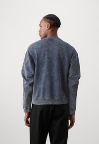 Blå bomullssweatshirt med en falmet utseende, med rund hals og drop skulder, supplert med ribbede mansjetter og kant.