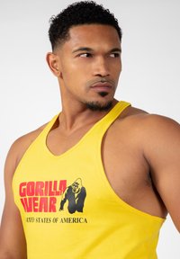 Rumena majica brez rokavov z napisom "GORILLA WEAR" in "UNITED STATES OF AMERICA" v rdeči barvi ter grafiko črnega gorile. Mehka tkanina.