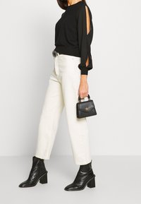 Top negro de manga larga con detalles recortados, combinado con pantalones anchos blancos, botas negras hasta el tobillo y un pequeño bolso negro texturizado.