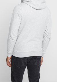 Sudadera con capucha gris de textura suave, con capucha ajustable y puños acanalados. Combinada con jeans oscuros de corte slim.