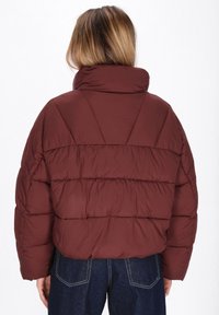 Giacca puffer bordeaux con colletto alto, caratterizzata da un design trapuntato e una silhouette oversize. Tessuto morbido, con cuciture pronunciate e una vestibilità cropped.