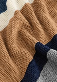 Texturerad filt med flera färger: mörkblå, ljusbrun, kräm och grå, i ett ribbat mönster med synliga stygn.