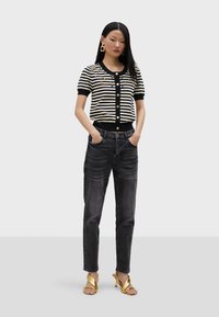 Crno-bijeli prugasti pulover kratkih rukava s gumbima sprijeda i cvjetnim ukrasima, u kombinaciji s tamnim trapericama i zlatnim potpeticama.