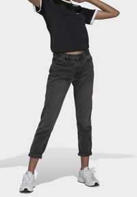 Svart kortärmad topp med vita detaljer, tillsammans med högmidjade mörkgrå jeans upplupna vid fållarna, kompletterat med vita träningsskor.