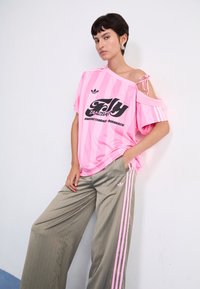 Roosa triibuline lühikeste varrukatega T-särk musta graafikatekstiga, koos laiadest hallidest pinstriped pükstest roosa külgribaga.