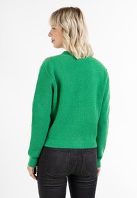 Maglione verde a coste con maniche lunghe e scollatura rotonda, caratterizzato da un design corto e materiale a maglia testurizzato. Pantaloni neri aderenti.