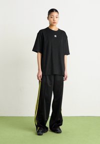 Black oversized t-shirt with a small logo, paired with black track pants featuring yellow side stripes, made of smooth fabric.