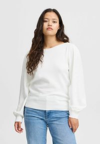 Weißer, gestrickter Pullover mit weitem Ausschnitt und langen, puffartigen Ärmeln, kombiniert mit hellblauen, geraden Jeans. Sanfte Textur, lässige Passform.