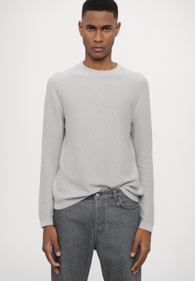 Hellgrauer Strickpullover mit strukturiertem Muster, Rundhalsausschnitt und langen Ärmeln, kombiniert mit dunkelgrauen Jeans.