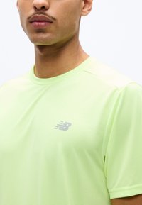 Κοντινό πλάνο ενός ατόμου που φοράει αθλητική μπλούζα New Balance ανοιχτού πράσινου χρώματος, εμφανίζοντας τον λαιμό, το κάτω μέρος του προσώπου και το πάνω μέρος του κορμού.