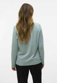 Maglione azzurro chiaro con maniche lunghe, orlo e polsini a costine, realizzato in un materiale morbido, visto da dietro.