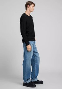 Suéter de punto negro, de ajuste holgado, combinado con jeans de mezclilla azul claro. La modelo lleva zapatos negros con suela gruesa. Diseño simple, con detalles mínimos.