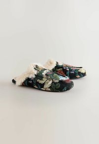 Slip-on slippers met een bloemenpatroon, gemaakt van zwart geweven stof, met een witte nepbontafwerking en een afgeronde neusvorm. De zool is plat en textuur.
